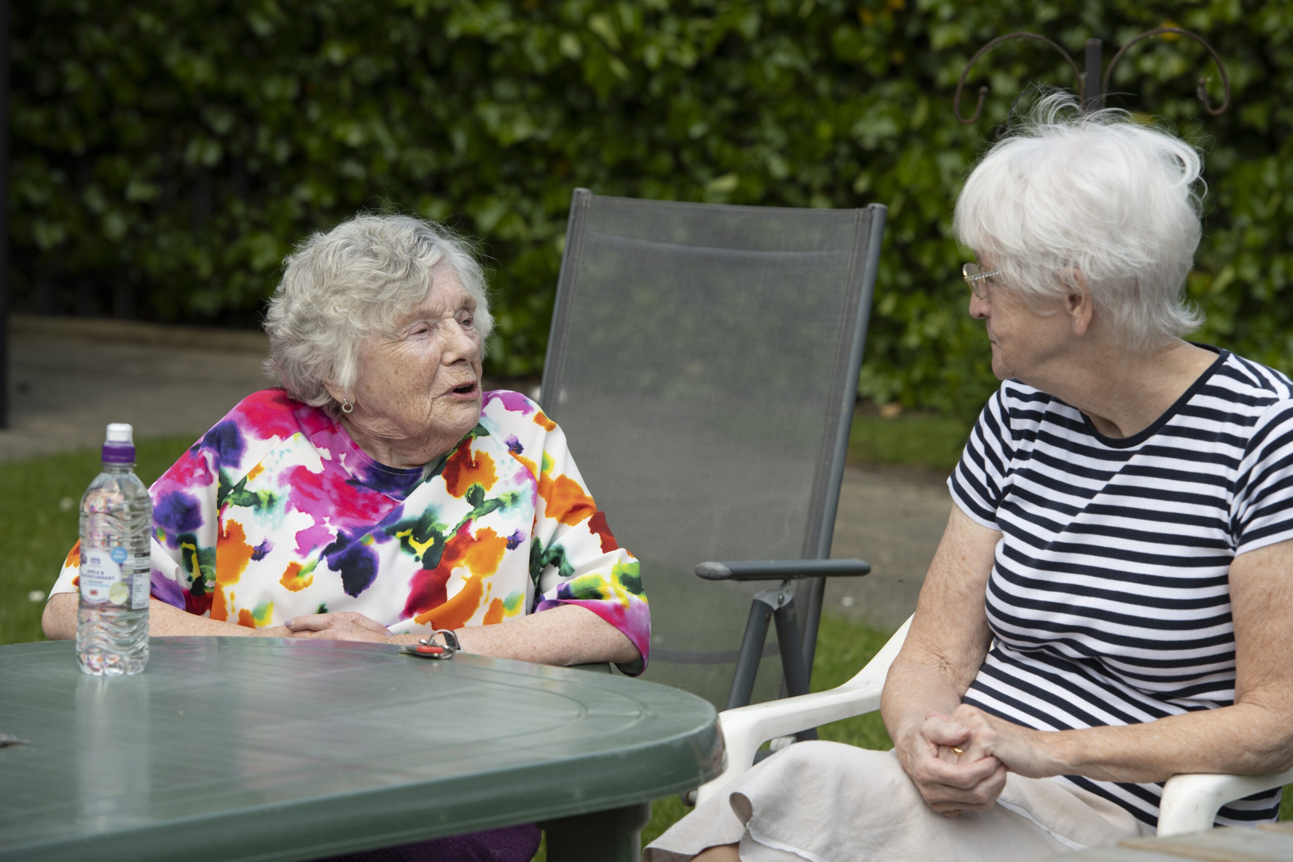 Two elderly women sat on garden chairs talking