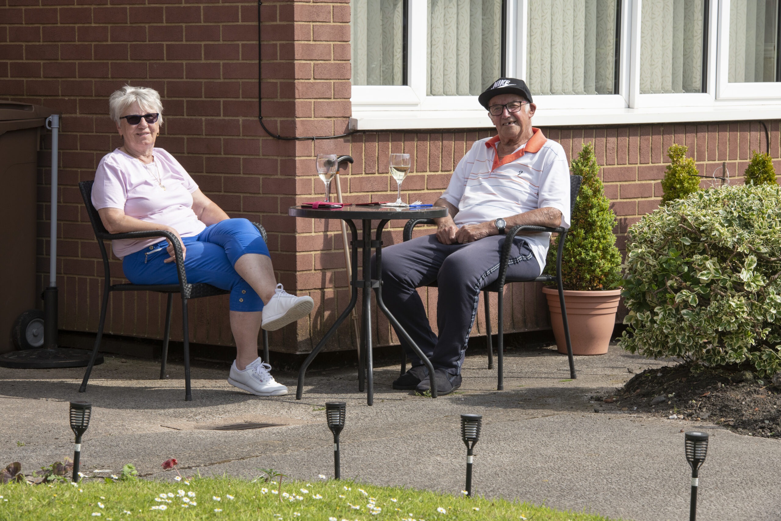 Elderly man and woman sat in the garden with glasses of wine