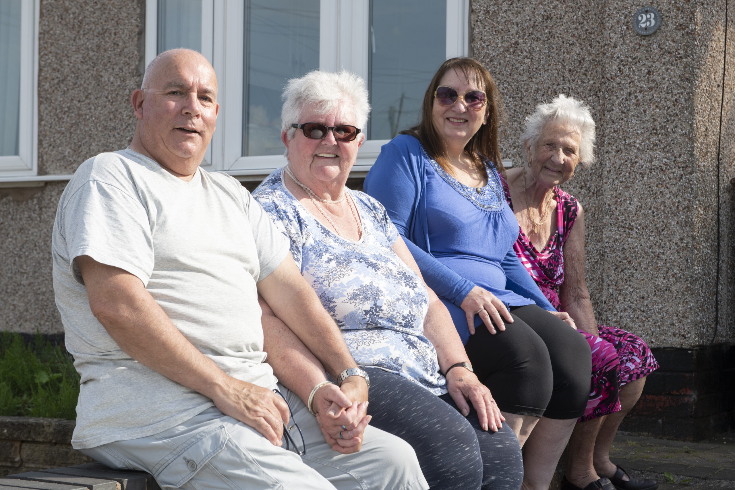 Group photo of three women and a man sat on low garden wall